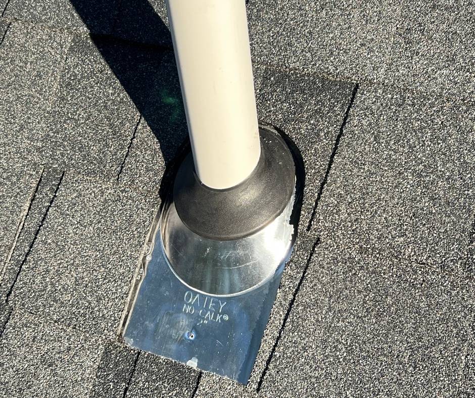 A white pipe is sitting on top of a gray roof.