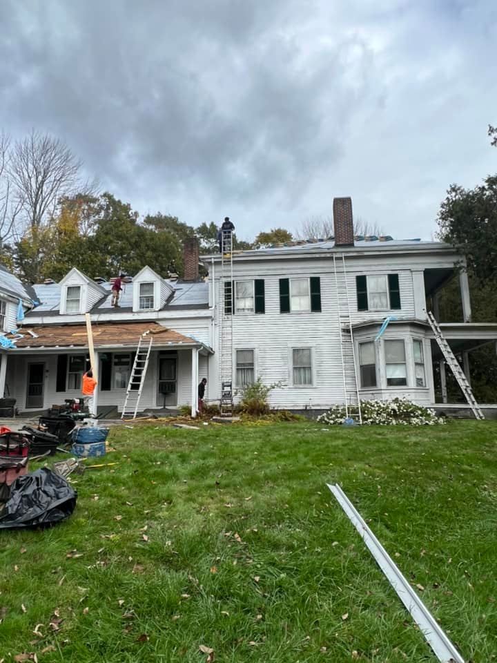 A man is standing on a ladder on the roof of a house.