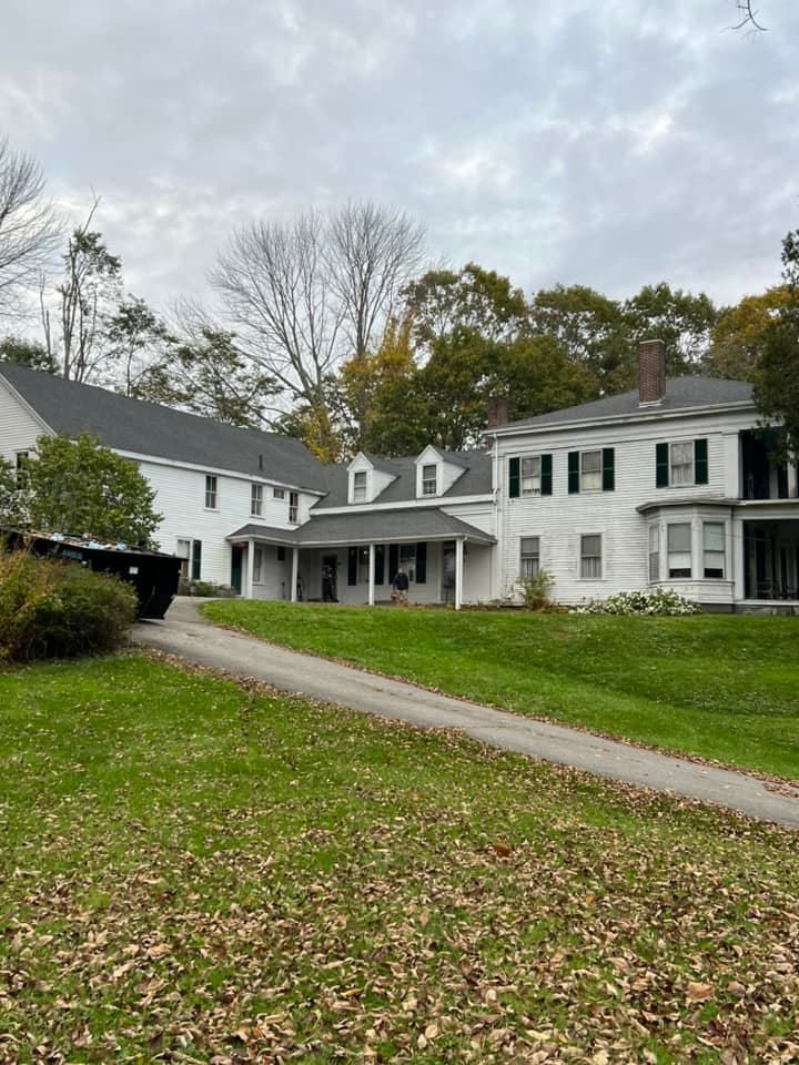 A large white house with a black roof is sitting on top of a lush green field.