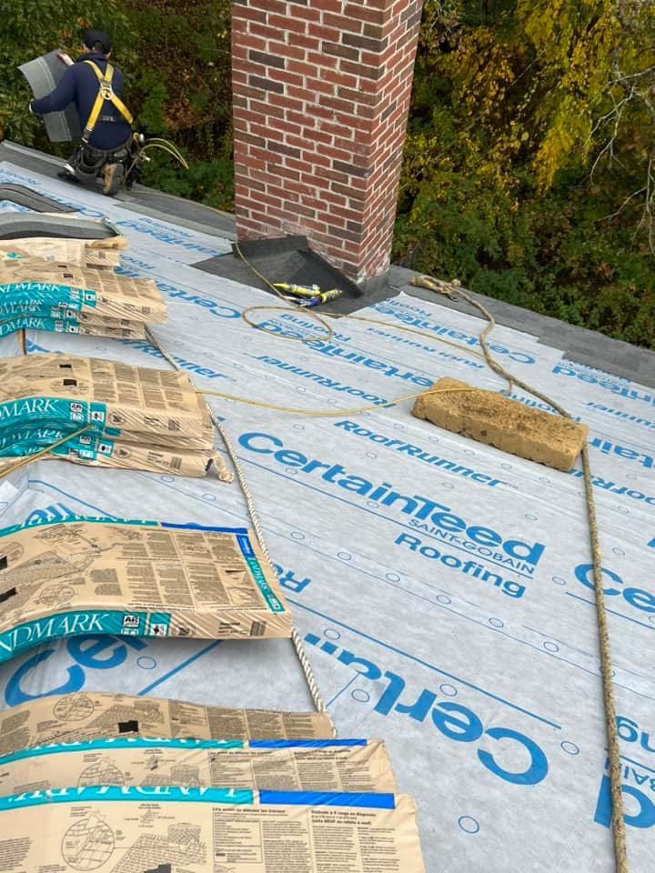 A man is working on a roof with a brick chimney in the background.
