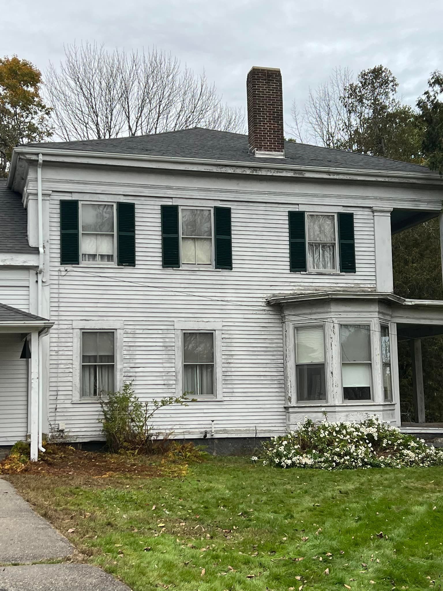 An old white house with black shutters and a chimney.