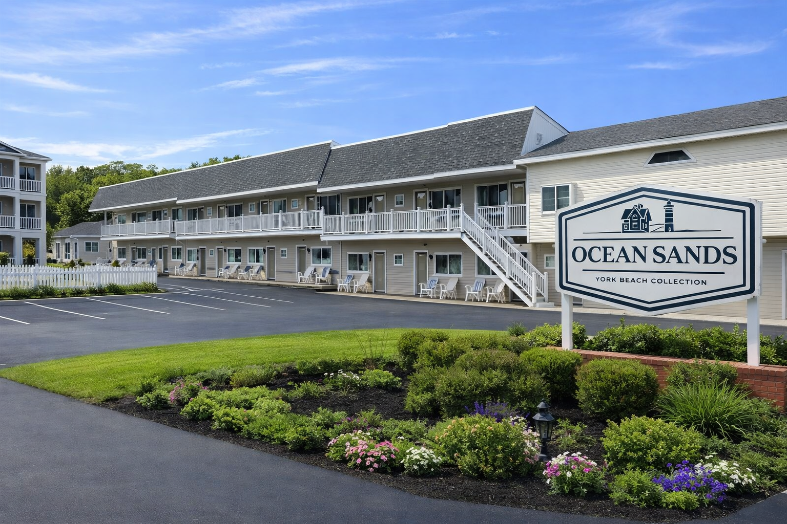 Ocean Sands motel featuring a two-story gray building, a large parking lot, and a prominent sign against a blue sky.