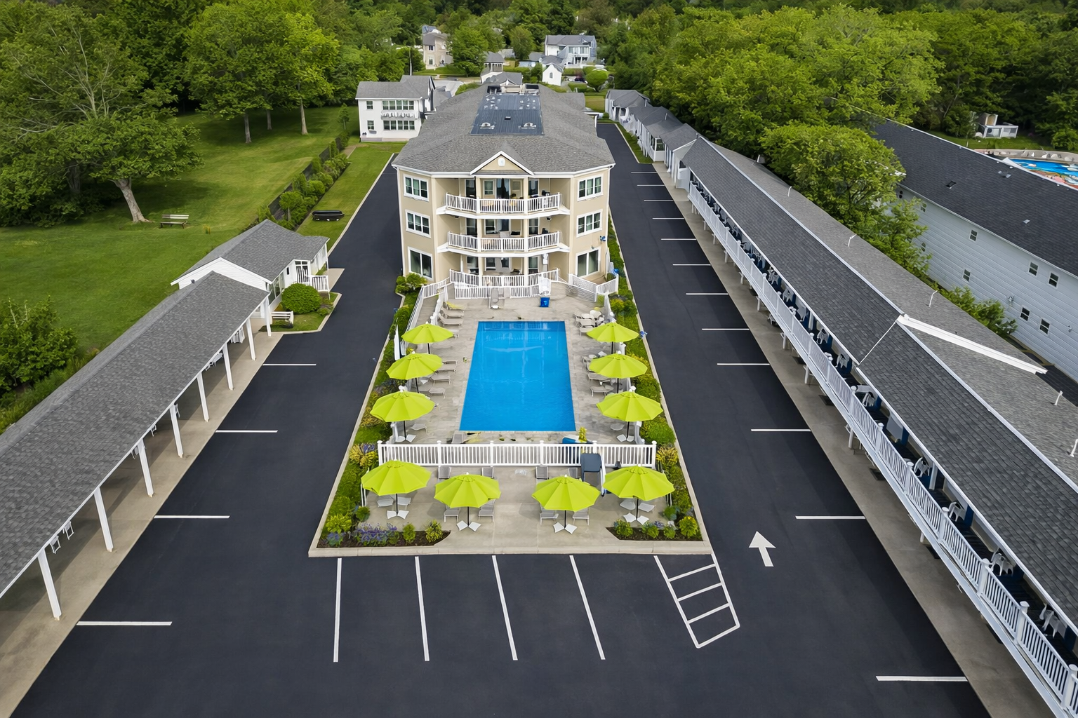 Aerial view of a motel complex featuring a central swimming pool surrounded by lime green umbrellas and paved parking.