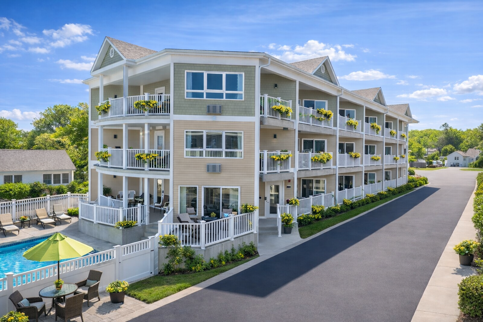 A three-story hotel with beige and green siding, private balconies, and an outdoor swimming pool on a sunny day.
