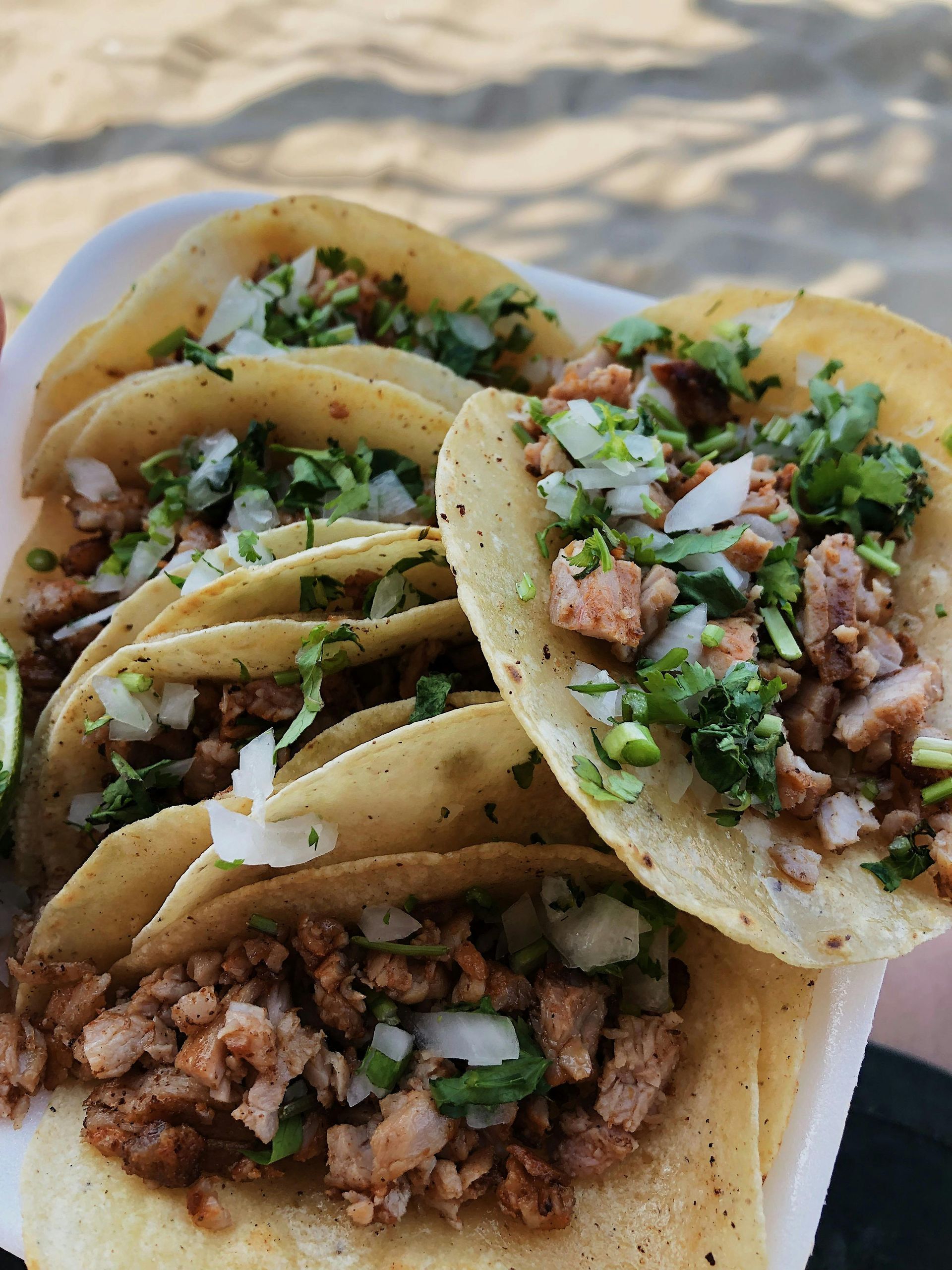 Several street-style tacos with seasoned meat, chopped onions, and cilantro served on a white plate.