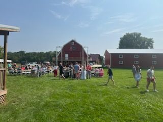 A group of people are standing in a grassy field in front of a barn.