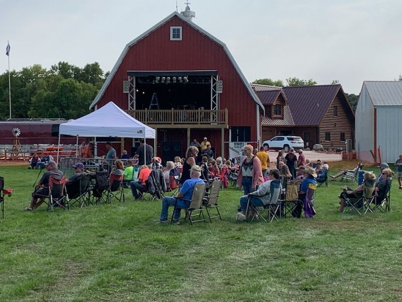 A group of people are sitting in chairs in front of a red barn.