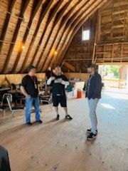A group of men are standing in a barn talking to each other.