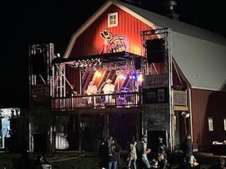 A group of people are standing in front of a red barn at night