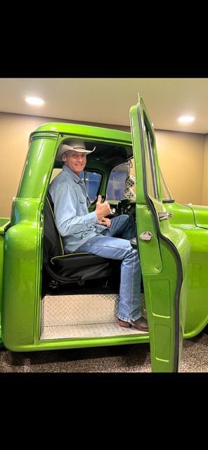 A man in a cowboy hat is sitting in the back of a green truck.