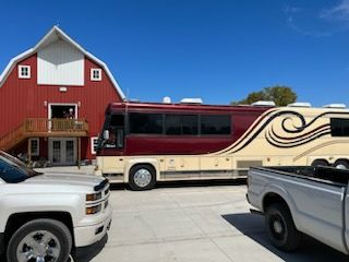 A truck and a bus are parked in front of a red barn.