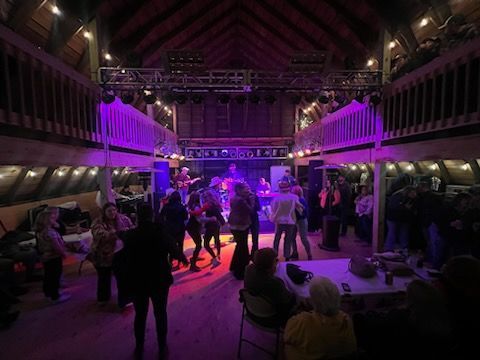 A group of people are dancing in a large room with purple lights.