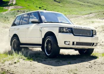 A white range rover is driving on a dirt road.