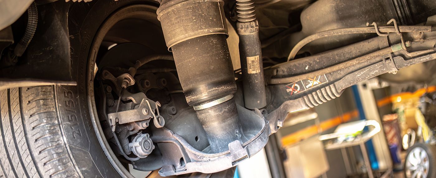 Undercarriage of a vehicle showing exhaust and suspension components over a mechanic’s bay