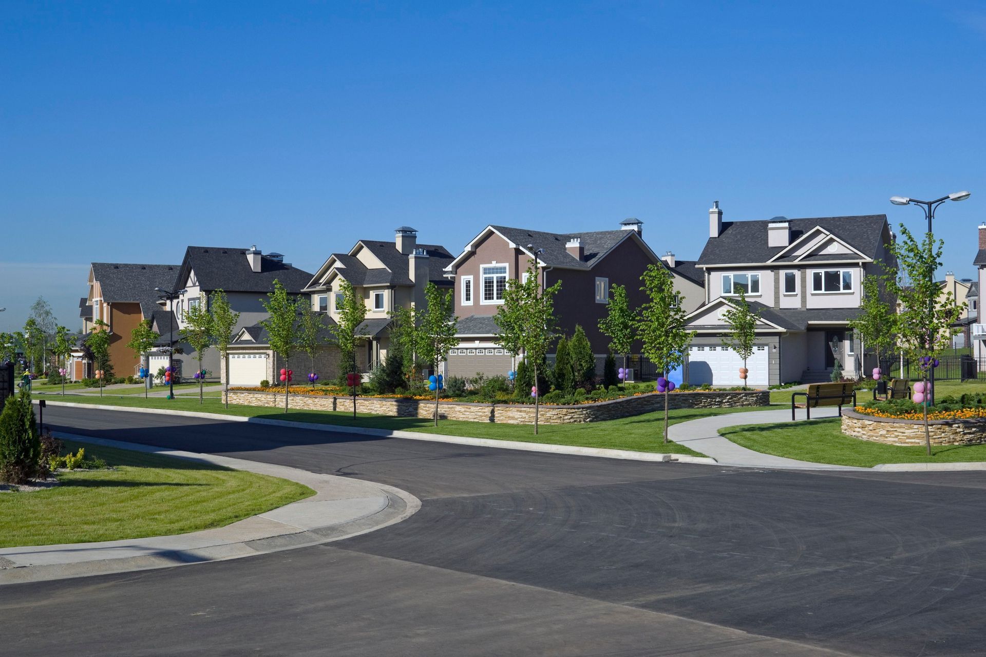 Curved suburban street with modern houses, trees, and landscaped lawns under a clear blue sky