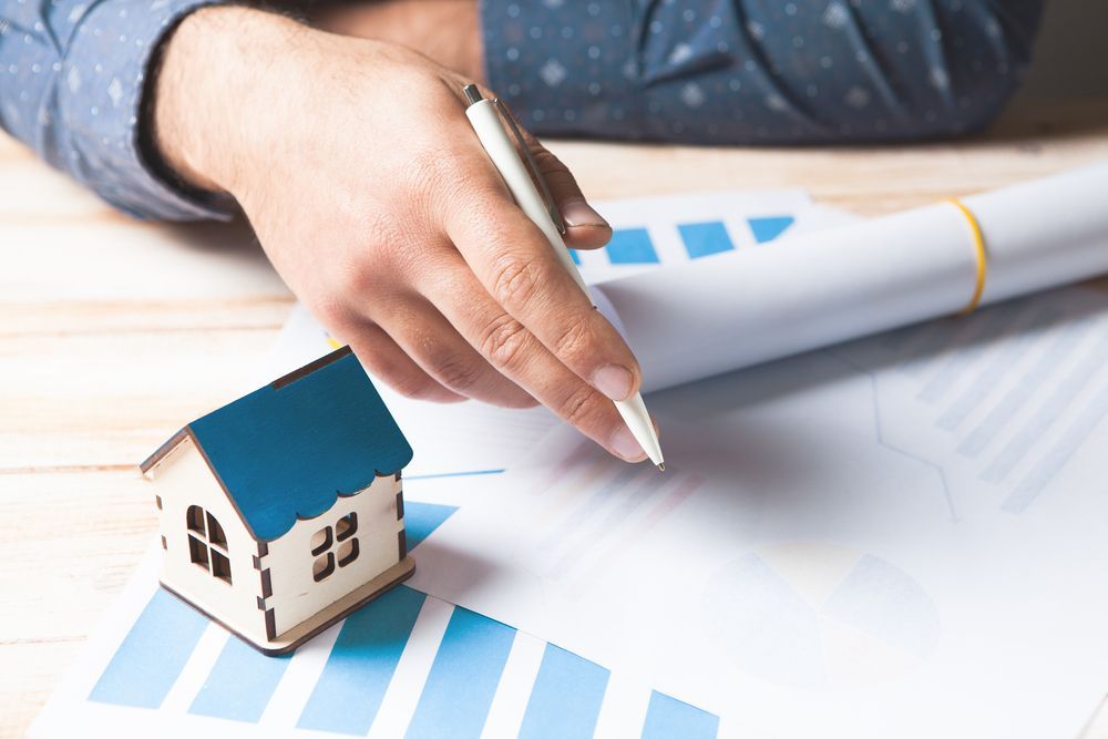 Hand holding pen over house model and blue charts on desk