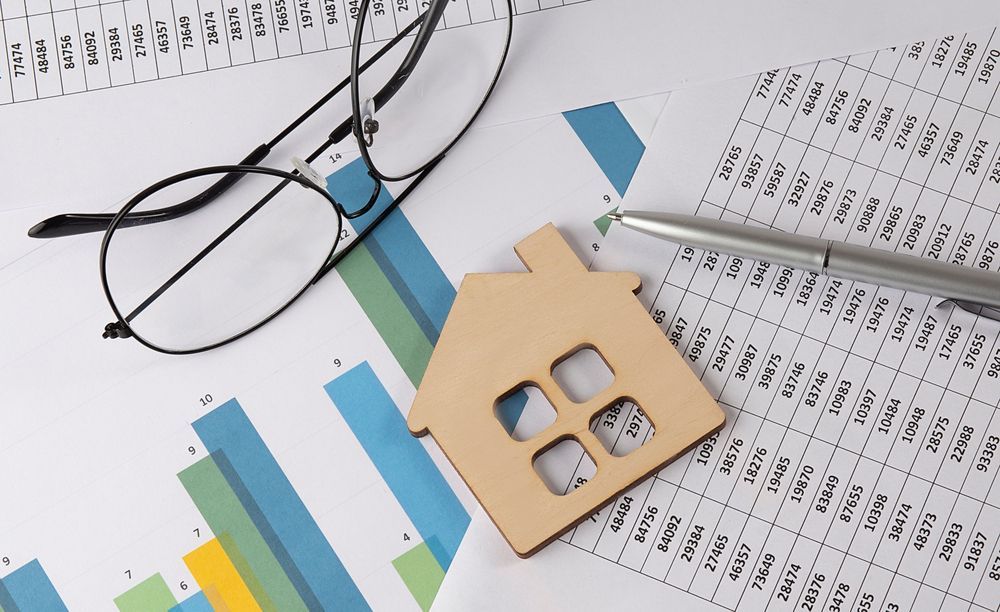 Glasses, house keychain, pen, and charts on a desk with financial documents