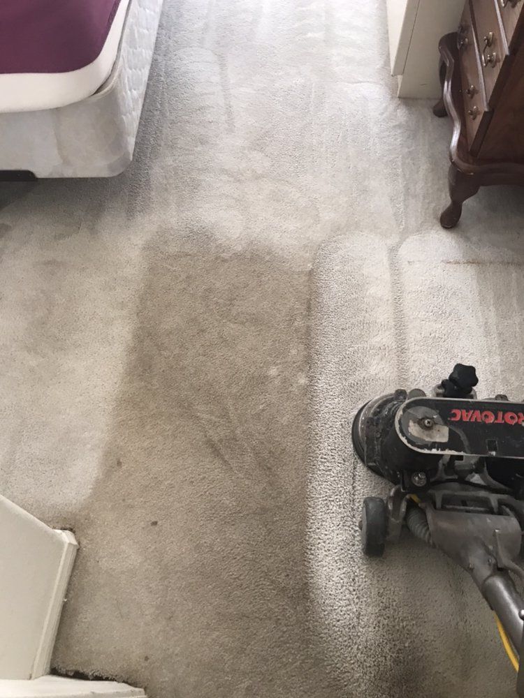A vacuum cleaner is being used to clean a carpet in a bedroom.