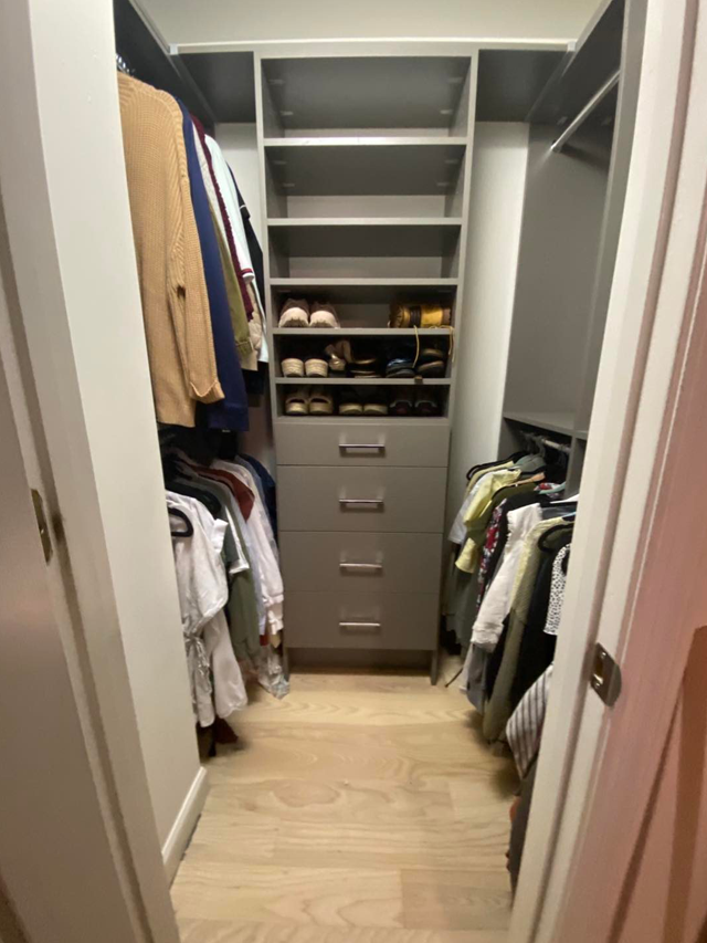 A small walk-in closet with shelves, drawers, and hanging clothes in light colors.
