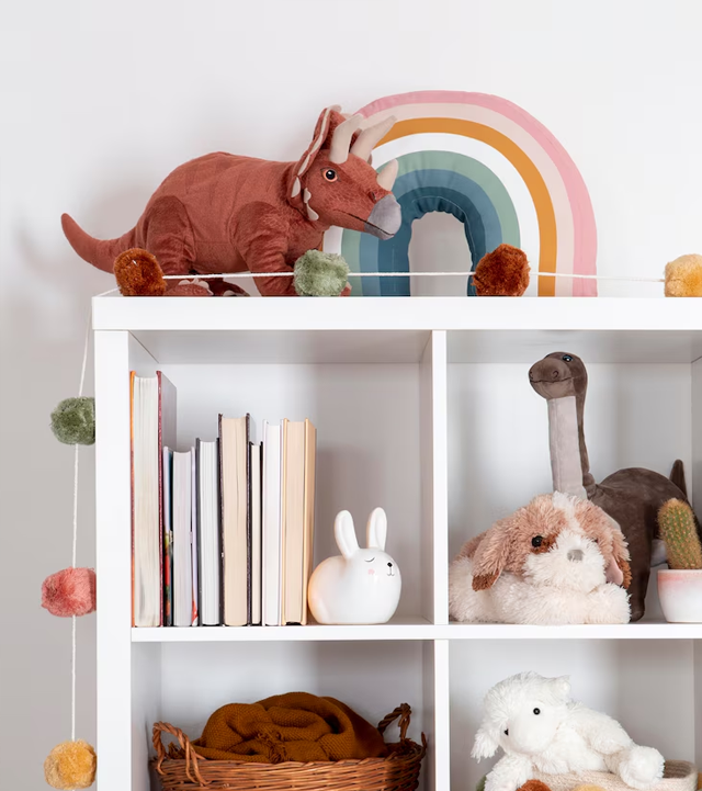 White cubby shelf with dinosaur, rainbow, books, and stuffed animals.