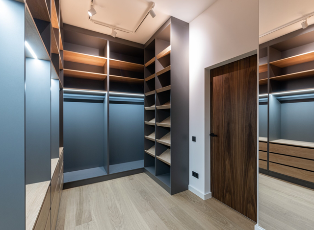 Walk-in closet with dark gray shelves, wooden floor, and a wood door on the right.
