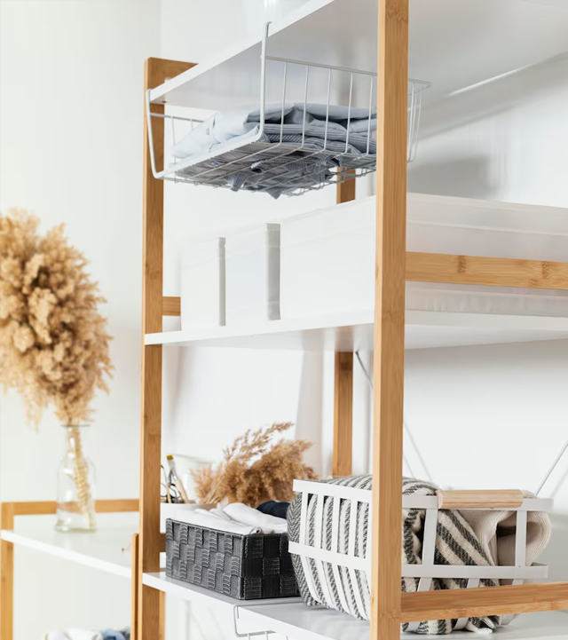 White shelving unit with bamboo frame, holding storage baskets and folded linens.
