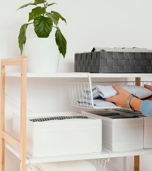 Person folding clothes into a white wire basket under a shelf; white and gray storage on the shelves.