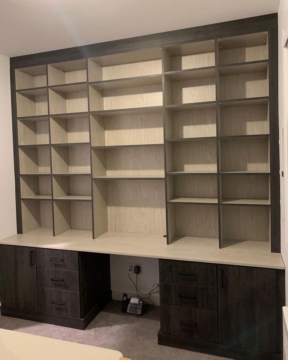 Built-in bookshelf and desk in a room. Dark gray cabinets and shelves, light wood shelves and desk surface.