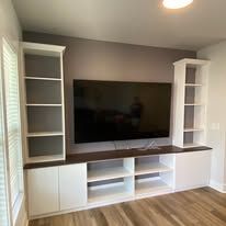 Built-in entertainment center with TV, white cabinets, brown countertop, and bookshelves on either side.