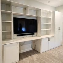 Built-in white wall unit with a desk, shelves, and a mounted TV.