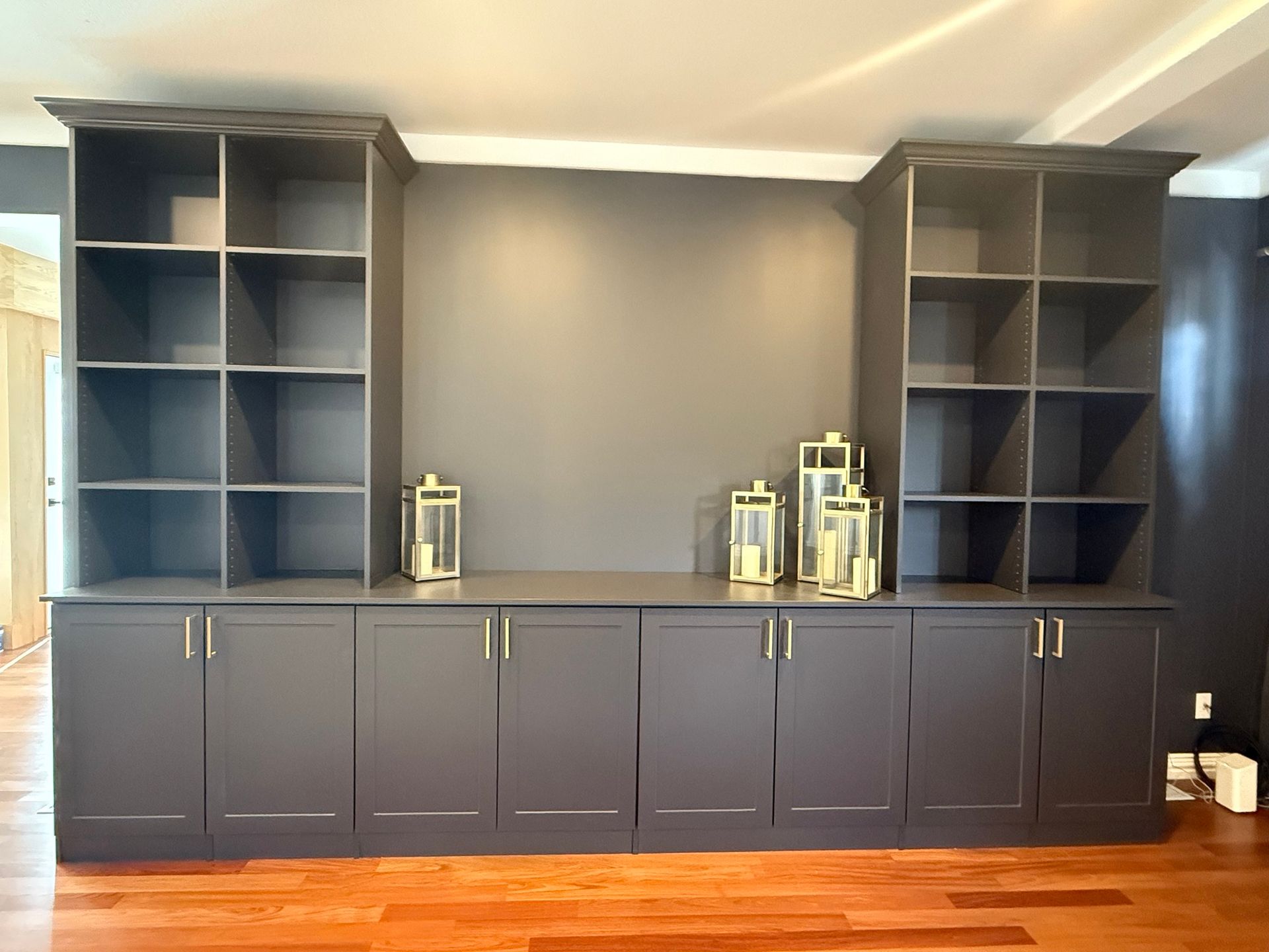 Dark gray built-in cabinet with bookshelves and storage cabinets. Gold lanterns sit on the countertop.