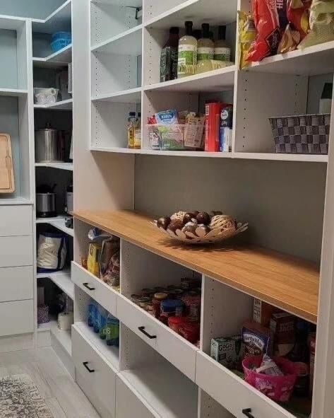 White pantry with wooden countertop, shelves stocked with food items, and drawers.