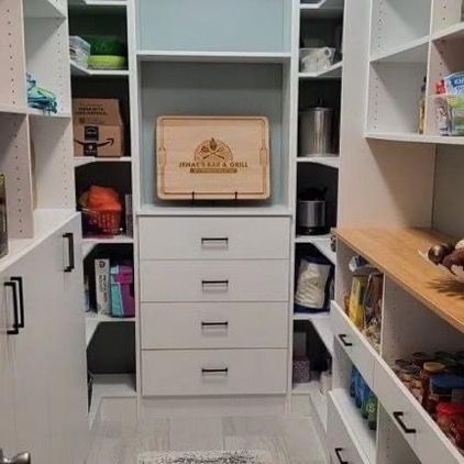 White pantry with shelves, drawers, and a wooden counter holding jars and food items.
