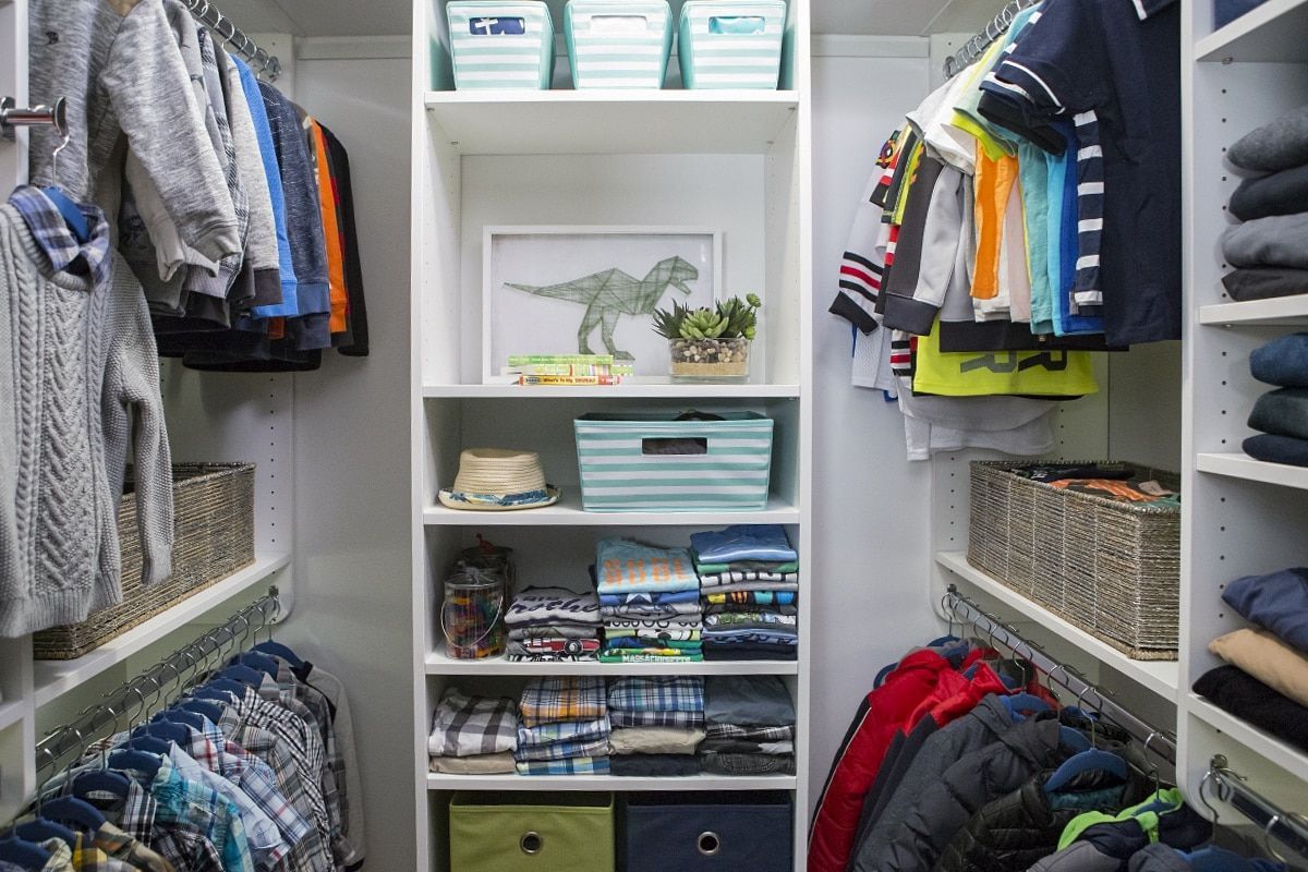 A child's organized closet with hanging clothes, folded items, and storage bins; white shelves.