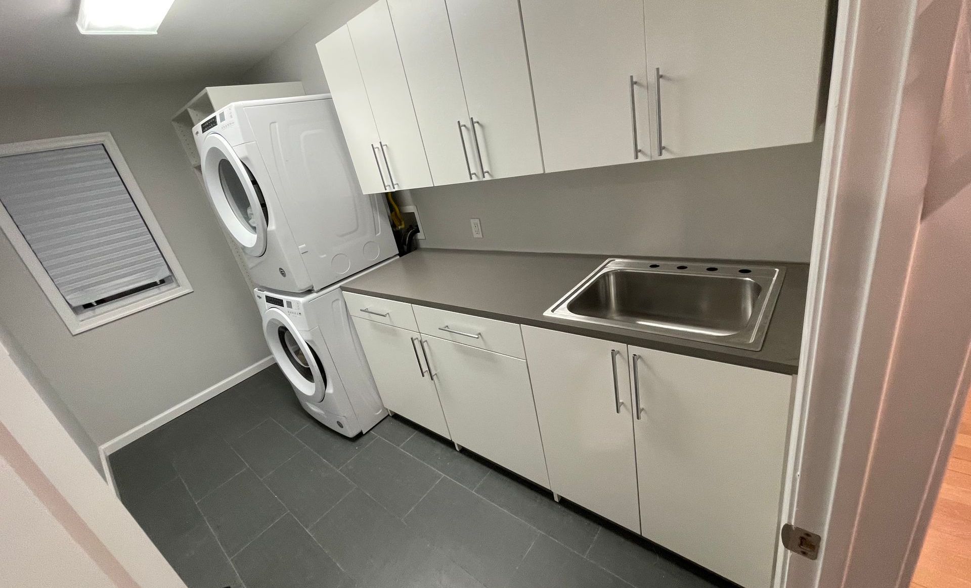 Laundry room with stacked white washer and dryer, white cabinets, and a sink.