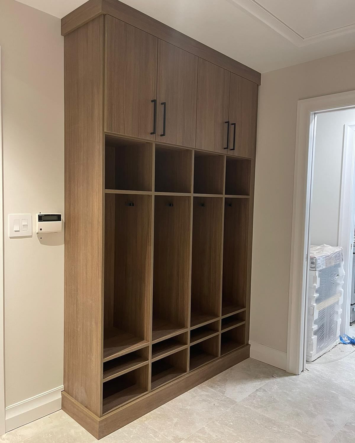 Tall wooden storage unit with lockers, cubbies, and shoe storage, built-in against a wall.