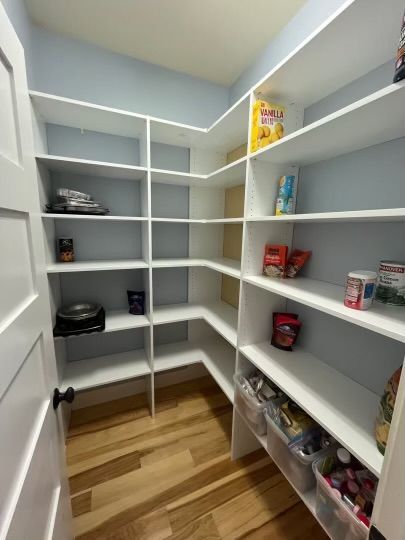 White pantry with shelves, wooden floor, and light blue walls.