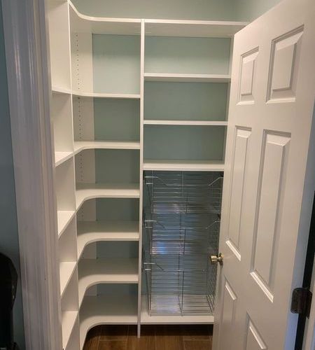White pantry with built-in shelves and a pull-out wire basket system. A white door is on the right.