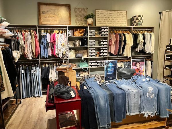 Clothing store interior with racks of clothing, jeans on a table, and decorative wall art.
