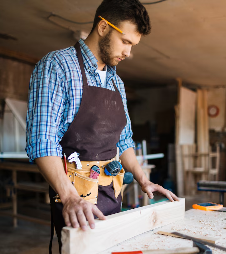 Carpenter in a workshop, wearing an apron and tool belt, working with wood.