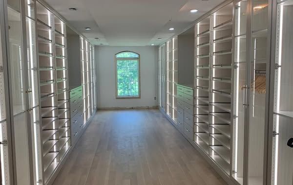 Walk-in closet with built-in shelving and drawers, illuminated by LED lights. A window is at the end of the room.