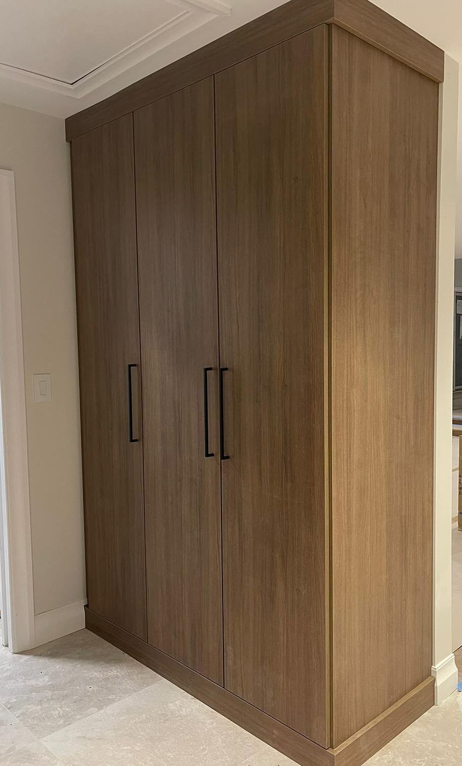 Wooden wardrobe with four doors, dark hardware, in a room with light-colored walls and carpet.