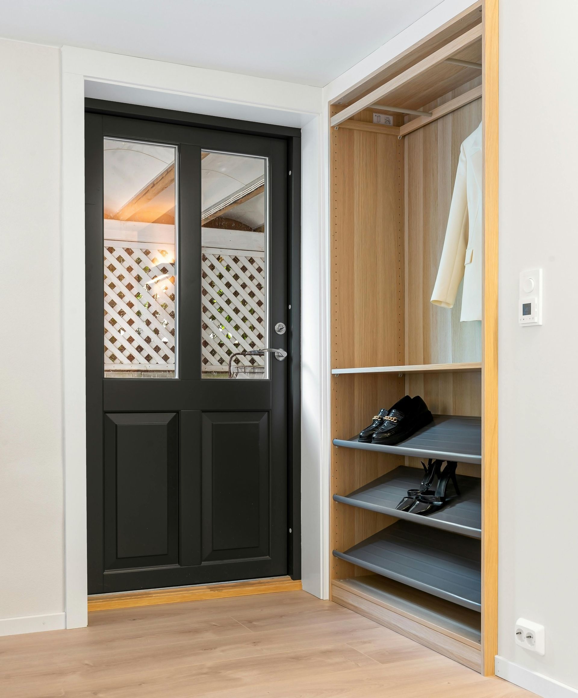 Black door with latticed windows next to a wooden closet with shoes and coat.