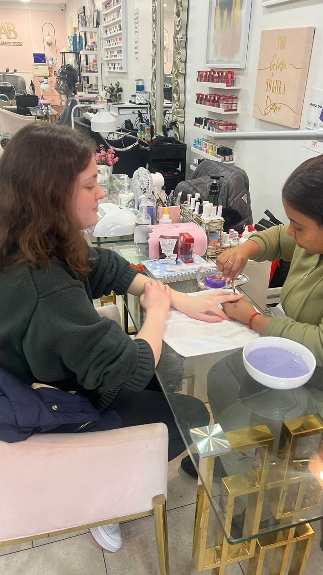 Two women are sitting at a table in a salon getting their nails done.