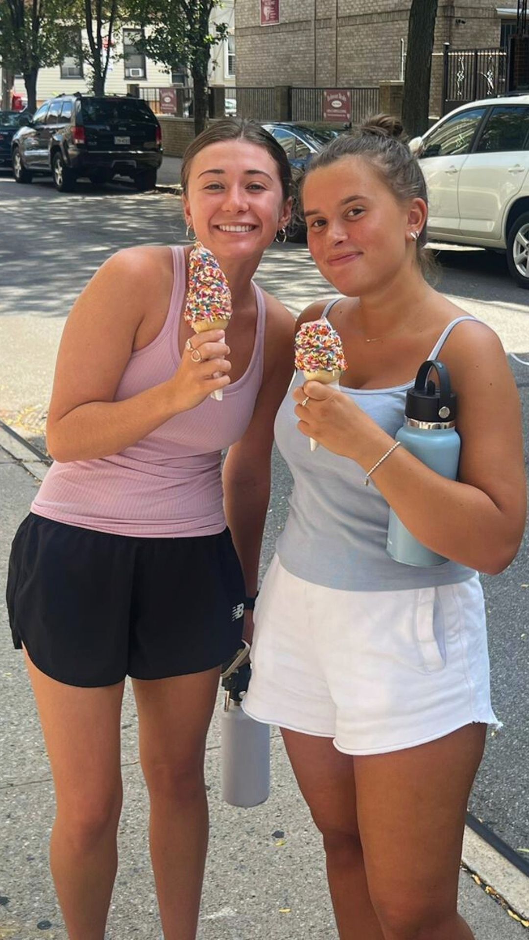 Two women are standing next to each other eating ice cream cones.