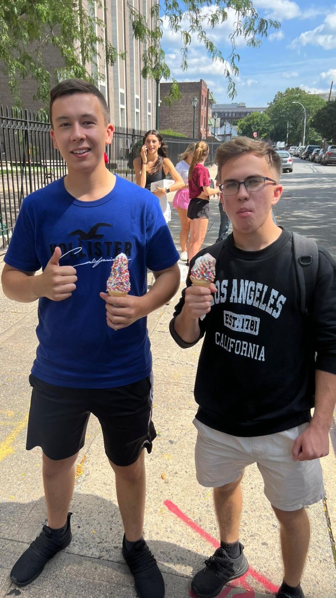 Two young men are standing next to each other holding ice cream cones.