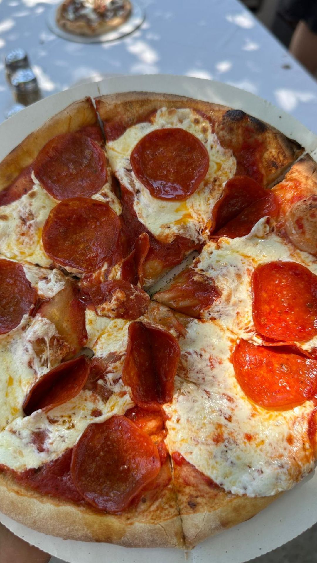 A person is holding a pepperoni pizza on a paper plate.