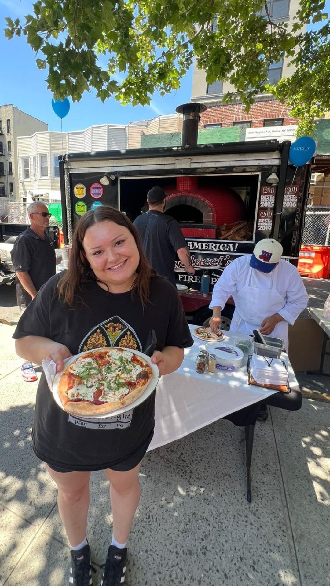 A woman is holding a pizza in front of a pizza truck.