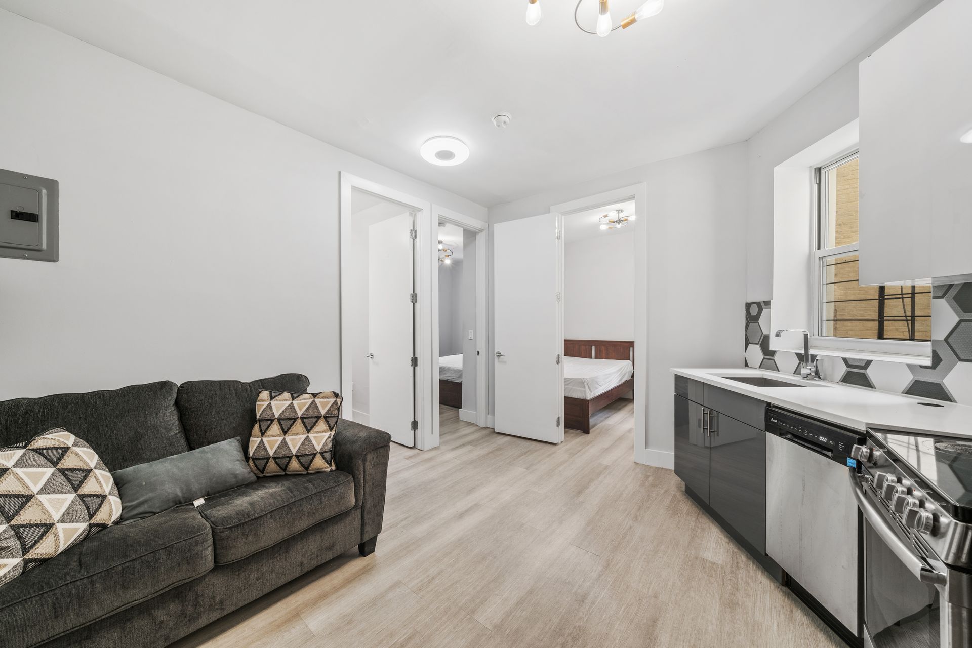 A living room with a couch and a kitchen with a bed in the background.