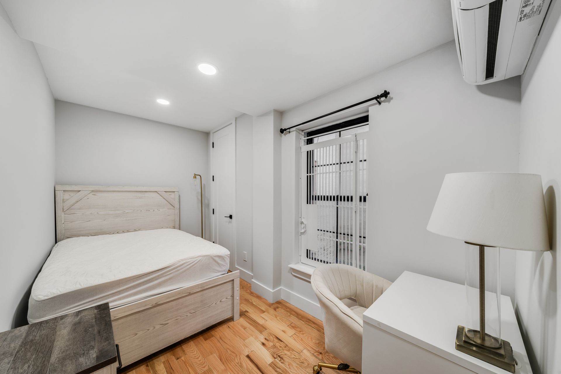 A bedroom with a bed , chair , desk , lamp and air conditioner.
